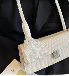Dettaglio borsa baguette crema con texture a onde, bordo in pizzo e fibbia con strass