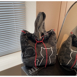 Detail of grey denim tote bag featuring white cat embroidery and red rope drawstring