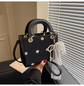 Detail of black daisy handbag featuring lace pearl bow charm and gold hardware accents