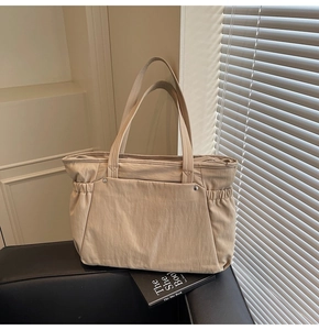 Vue détaillée du grand sac cabas beige avec plusieurs poches sur un canapé en cuir