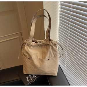 Detail of beige nylon tote bag featuring drawstring closure and magnetic buckle design