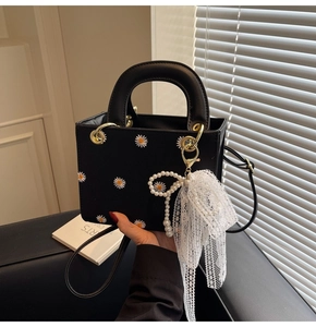 Detail of black box bag featuring white daisy embroidery and pearl lace bow charm