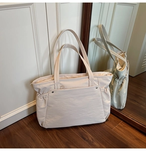 Détail du sac cabas en toile beige avec poche frontale rivetée et poches latérales à cordon