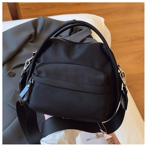 Detail of black waterproof nylon crossbody bag with silver hardware on white fabric