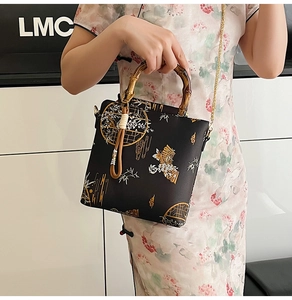 Detail of black silk oriental handbag featuring bamboo handle and golden floral patterns