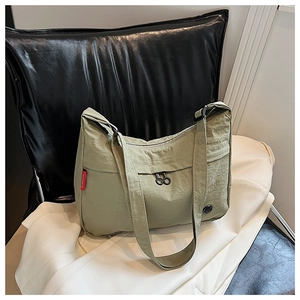 Detail of light olive nylon bag featuring a side red label and a zipper front pocket
