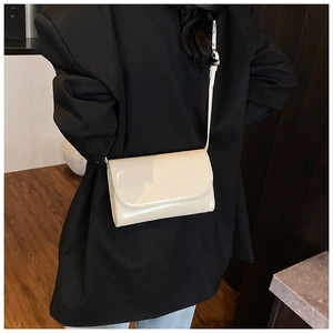 Minimalistische roomwitte glanzende crossbodytas getoond op een model met blazer