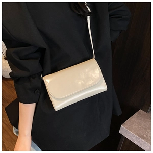 Detailopname van de minimalistische beige glanzende schoudertas bij een model