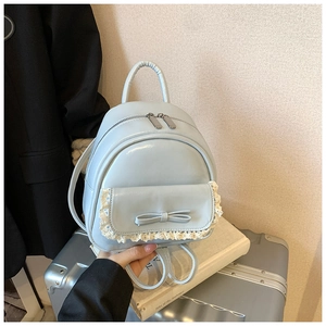 Detail eines hellblauen Mini-Rucksacks mit Schleife und Spitze auf silbernem Koffer