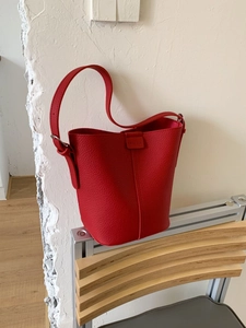 Classic red leather bucket bag with litchi texture on a wooden chair for daily commute