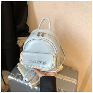 Detail eines hellblauen Rucksacks mit Schleife und Spitze auf silbernem Koffer