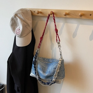 Detail of light blue denim bag featuring red striped rope strap and silver leather base