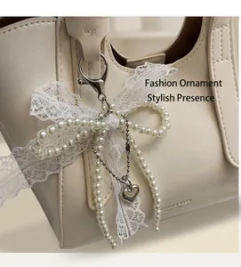 Detail of white pearl bow lace charm with silver heart pendant on a leather handbag