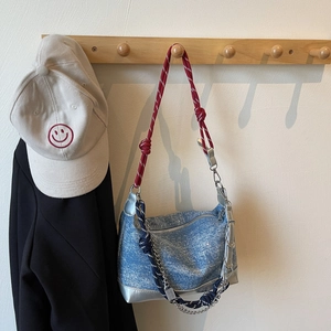 Blue denim tote bag with silver leather trim and red woven rope strap on wooden hook