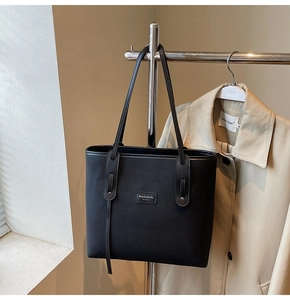 Detail einer schwarzen Twill-Tasche mit Markenplakette, kombiniert mit einem Trenchcoat