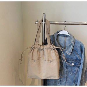 Detail of khaki nylon tote bag with drawstring closure and metal buckle front pockets