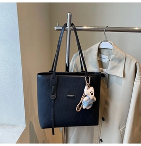 Detail einer großen schwarzen Tragetasche mit Twillstoff, Lederbesatz und süßem Teddybär-Anhänger