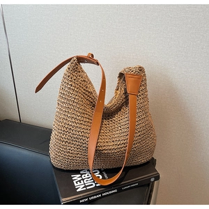 Dettaglio borsa tote in paglia naturale con spalline in pelle marrone sul divano