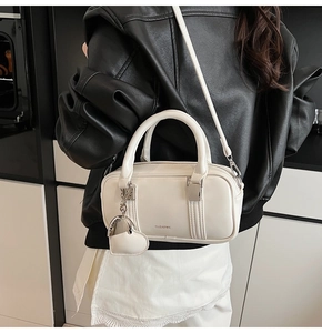 Close-up of white minimalist pillow bag with silver CLEAR K logo and heart charm