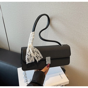 Dettaglio borsa in pelle nera testurizzata con chiusura argento e nastro in pizzo bianco