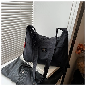 Detail of a black nylon crossbody bag with dual-zipper front pocket on a white sill