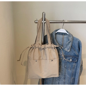 Detail of beige drawstring tote bag with dual front metal buckle pockets on hanger