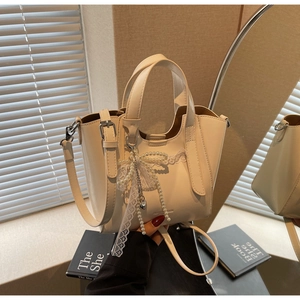 Detail of cream white leather bucket bag with pearl lace bow charm and fashion logo