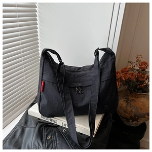 Detail of a black nylon shoulder bag showing metal dual zippers and a side red label