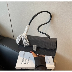 Dettaglio della borsa nera testurizzata con fiocco in pizzo bianco e fibbia di diamanti