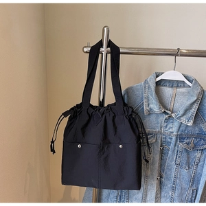 Detail of black drawstring tote bag with dual front pockets and silver snap buttons