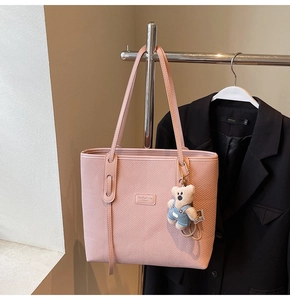 Detail der rosa geflochtenen Tragetasche mit Leder-Markenanhänger und süßem Teddybär-Anhänger
