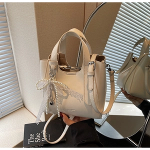 Detail of cream leather bucket bag with pearl lace bow and silver hardware on a mirror