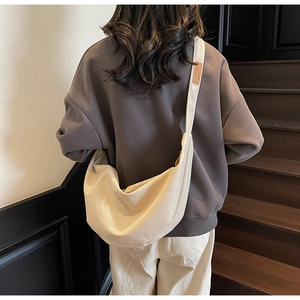 Close-up of beige canvas crescent bag with wide strap and brown leather label detail
