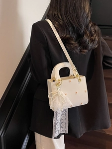 White leather handbag with daisy patterns and pearl charm, worn as a shoulder bag