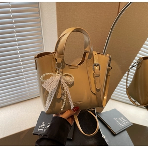 Detail of beige tote bag featuring elegant white lace bow and pearl pendant charm