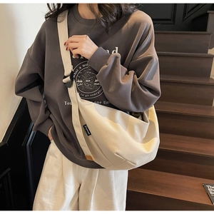 Close-up of beige canvas dumpling bag with adjustable strap worn on a casual outfit