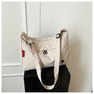 Detail view of beige nylon crossbody bag featuring red woven label and black zippers