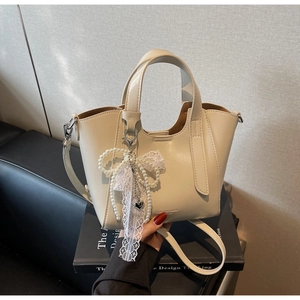 Detail of cream tote bag with pearl and lace bow charms on high-quality leather surface