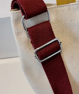 Détail d'un sac en toile beige avec bandoulière bordeaux réglable et boucle en argent