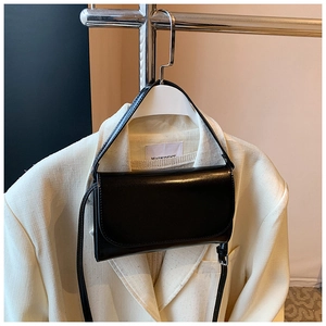 Minimalistische zwarte vierkante tas hangend aan een hanger met een witte blazer gestyled