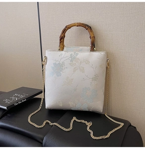 Close-up of floral embroidery on cream bag with bamboo handle and gold chain strap