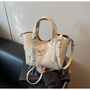 Detail of cream leather bucket bag featuring a pearl bow lace charm and adjustable strap