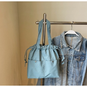 Detail view of light blue nylon drawstring tote bag with dual front pockets and metal buttons