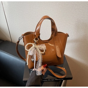 Detail of caramel glossy bucket bag with pearl bow charm and elegant lace strap detail