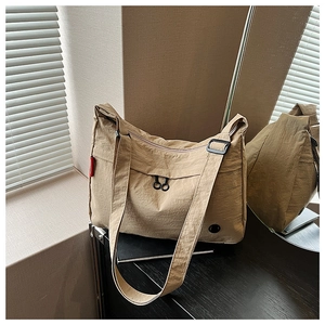 Detail of khaki nylon tote bag showing zipper sliders and textured fabric under sunlight
