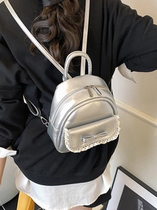 Silberner Mini-Rucksack mit weißem Spitzenbesatz und Schleife an einem Model getragen