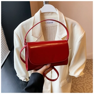 Detail van rode glanzende kunstlederen handtas met rechthoekige flap over een blazer