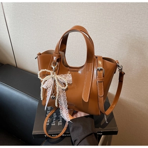 Close-up of glossy caramel bucket bag with delicate lace and pearl bow charm