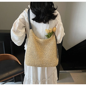 Dettaglio borsa in paglia intrecciata con tracolla in pelle su abito bianco