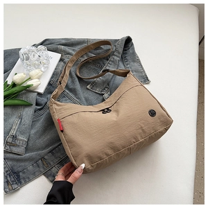 Detail of khaki nylon crossbody bag with adjustable strap and logo badge on white table